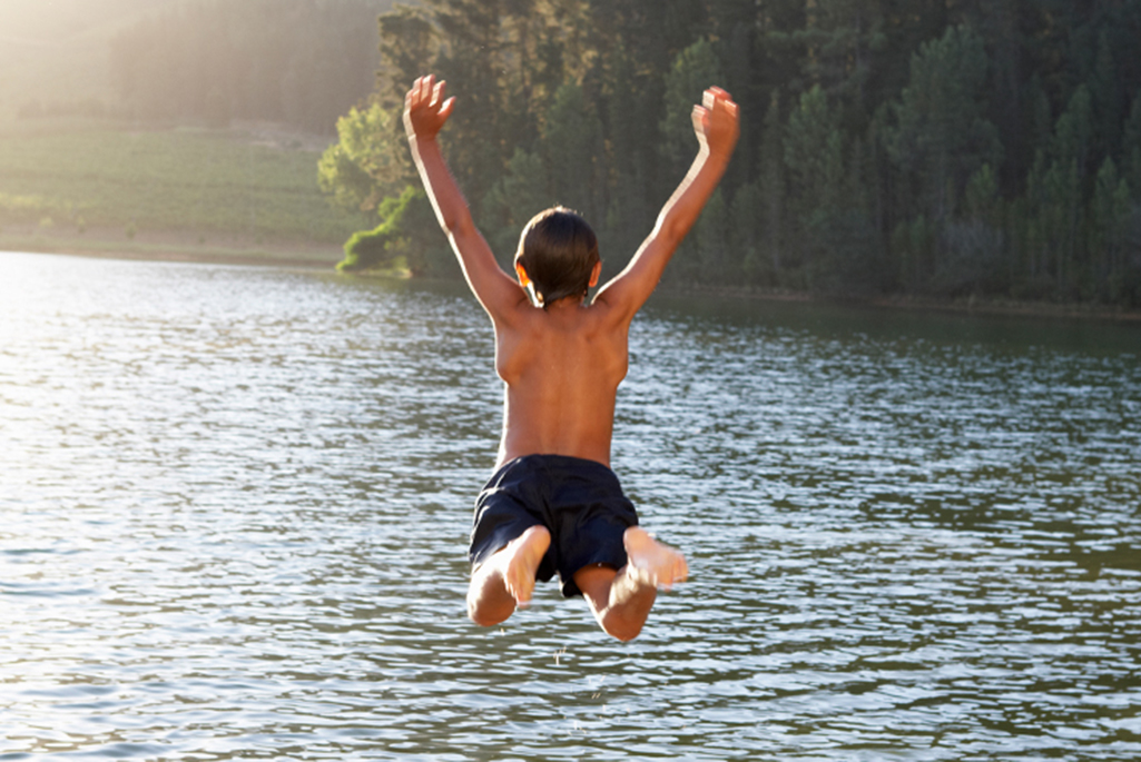 Pojke hoppar ner i vattnet för att bada.