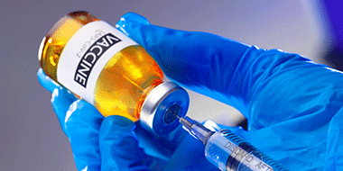 Foto av en hand i skyddshandske som fyller en spruta med coronavaccin från en ampull.