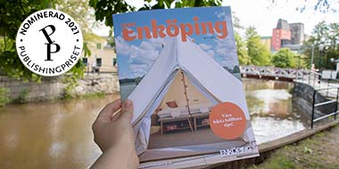 Foto på hand som håller upp tidningen Vårt Enköping. I bilden finns en rund illustration där det står "Nominerad 2021 Publishingpriset".